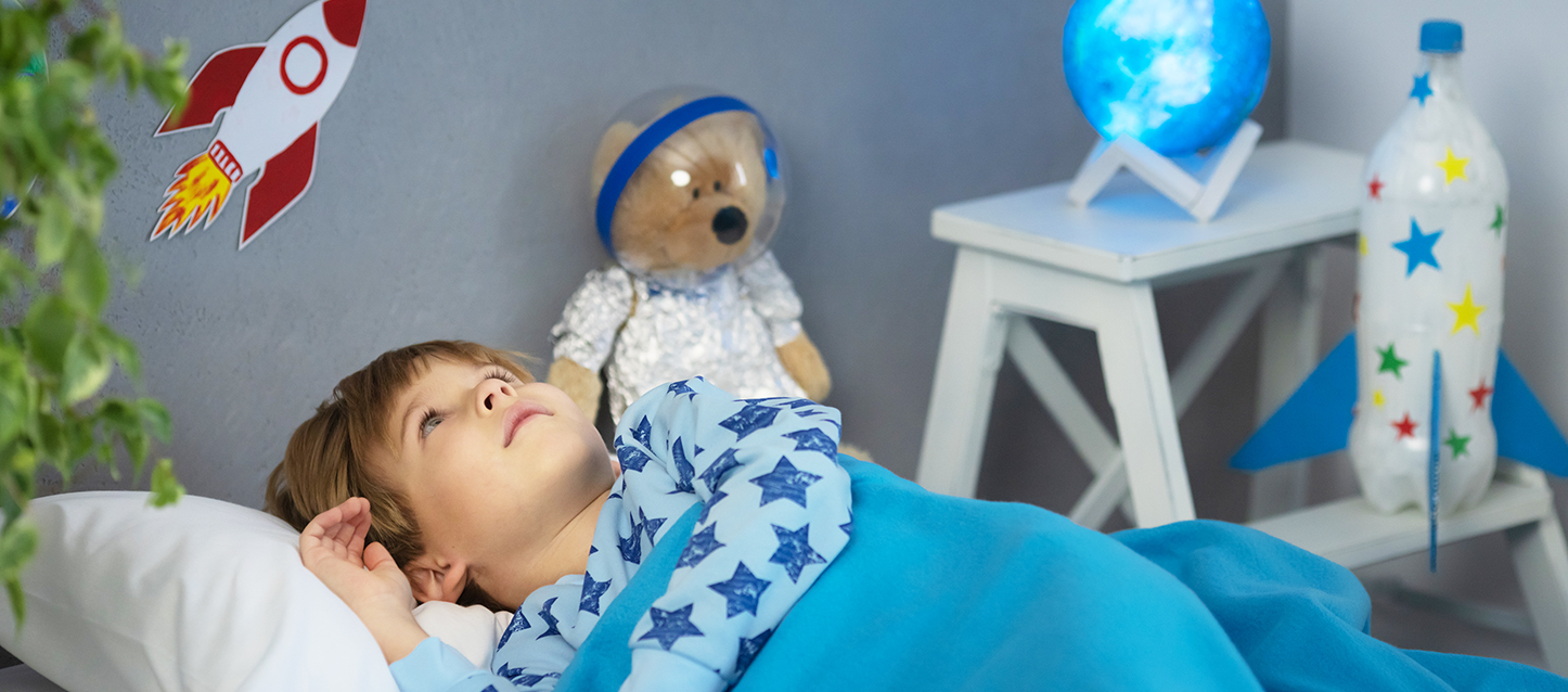 Enfant en bas âge dans une chambre d’enfant en pyjama bleu avec des étoiles bleu foncé couché dans son lit en regardant le plafond.