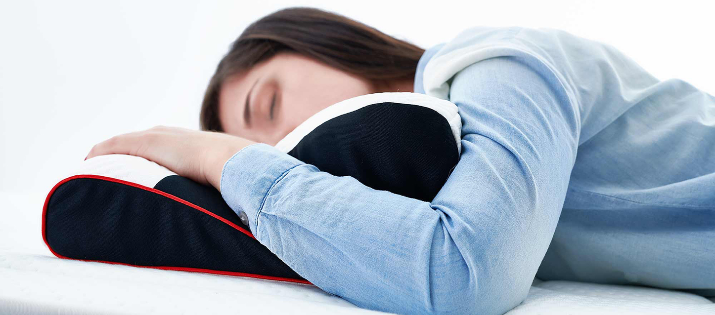 Fille brune aux cheveux longs vêtue d’une chemise en jean allongée sur le ventre sur un oreiller cervical avec son bras sur l’oreiller.