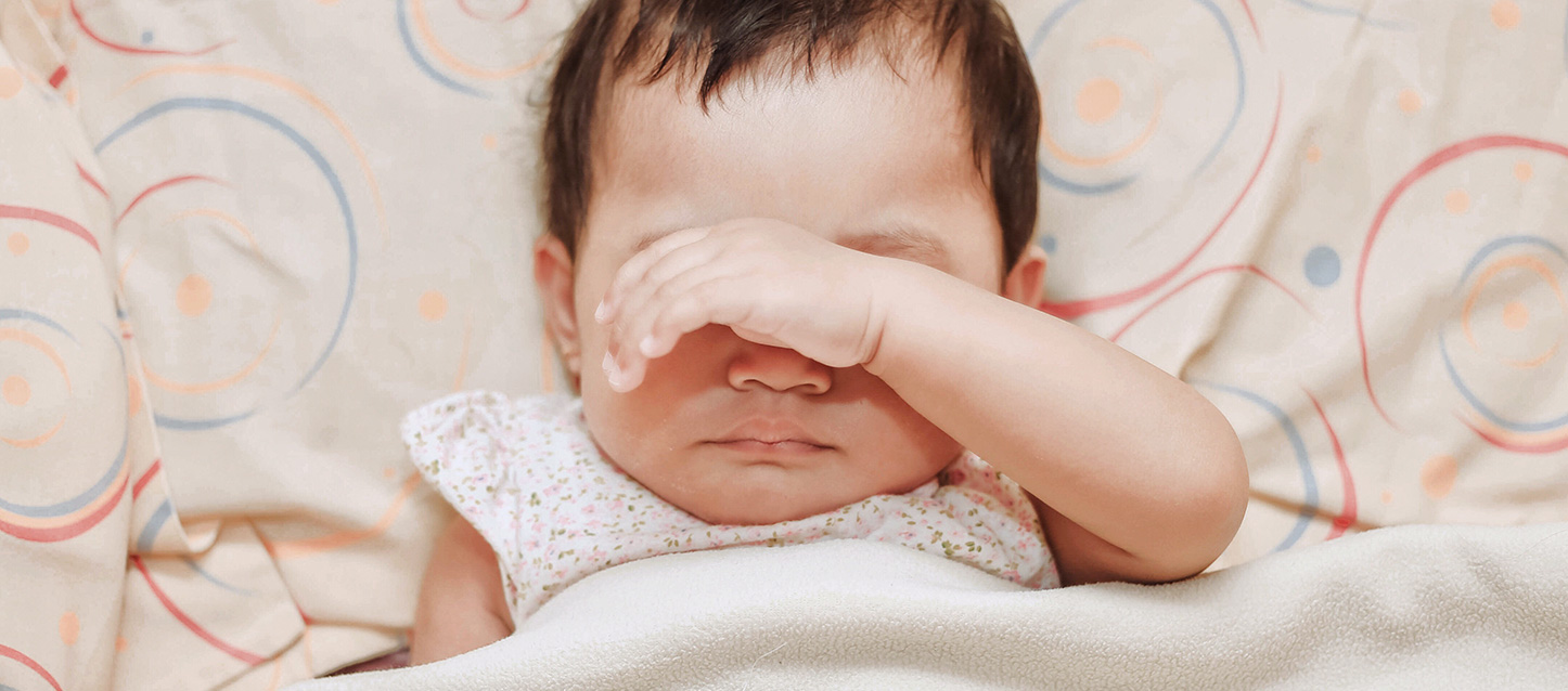 Bébé qui dort sur le dos avec une main sur son visage au niveau des yeux.