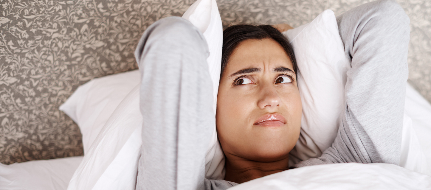 Femme allongée dans son lit qui regarde le plafond en faisant un geste de désapprobation.